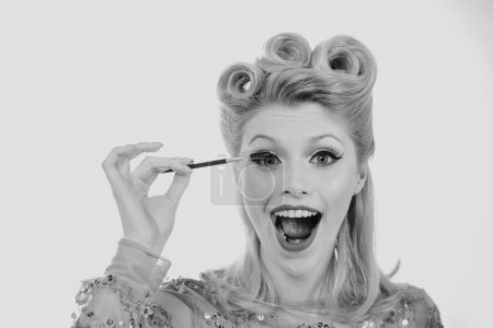 Foto de Maquillaje de cejas. Rubia mujer excitada cepillando cejas con cepillo de cejas primer plano. Pin up estilo - Imagen libre de derechos
