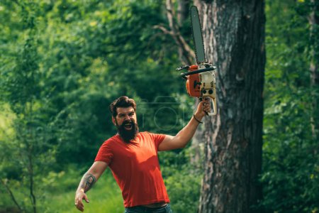 Foto de El leñador trabajando en un bosque. Trabajador de leñadores con motosierra en el bosque. Trabajador de madera parado en el bosque con motosierra. La tala. Agricultura y silvicultura - Imagen libre de derechos