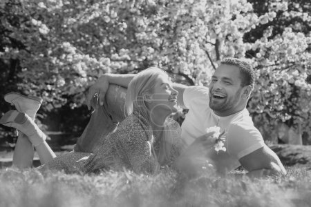 Foto de Feliz pareja de primavera enamorada de divertirse. Hermosos jóvenes amantes sonrientes disfrutando del jardín floreciente - Imagen libre de derechos