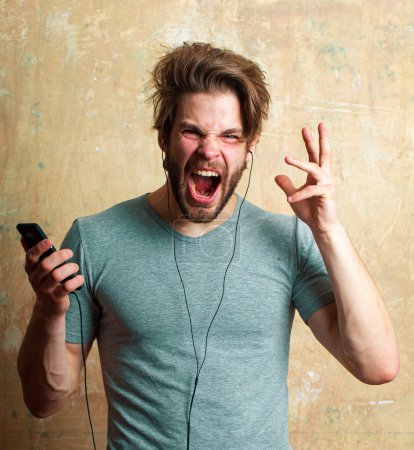 Téléchargez les photos : Homme excité écoutant de la musique avec smartphone. Homme surpris avec téléphone et écouteurs. Portrait émotionnel gars - en image libre de droit