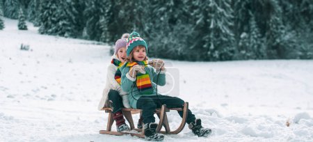 Foto de Niños felices en la nieve. Dos niños montan en un trineo retro de madera en un día de invierno. Invierno activo juegos al aire libre. Feliz Navidad concepto de vacaciones - Imagen libre de derechos