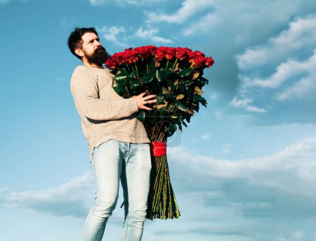 Photo for Celebrate Valentines Day Romantic Gifts and Valentines Gift Ideas. Handsome elegant man is holding bouquet of big red roses. Handsome man giving flowers to his lover on Valentines Day - Royalty Free Image
