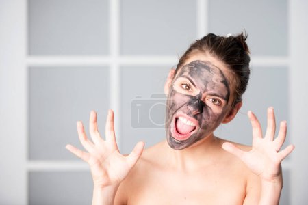 Téléchargez les photos : Femme avec masque facial charbon de bois. Belle jeune femme avec masque facial en terre cuite noire. Soins et traitements de la peau, spa, beauté naturelle et concept de cosmétologie - en image libre de droit