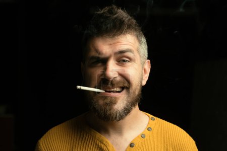 Foto de Hombre hipster barbudo fumando cigarrillo. Un hombre con mal hábito de salud. El chico no puede dejar de fumar. Deja de fumar cigarrillos. No elija el estilo de vida equivocado - Imagen libre de derechos