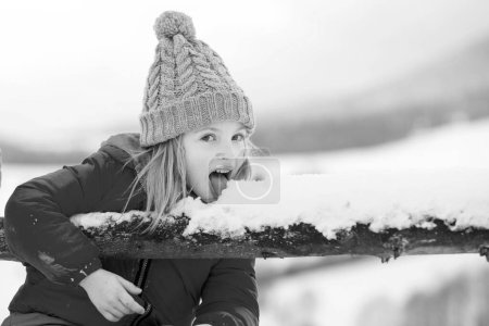Téléchargez les photos : Les enfants drôles mangent des flocons de neige. L'enfant lèche et mange de la neige en hiver. Des enfants avec des flocons de neige. Comique drôle visage - en image libre de droit