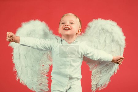 Photo for Excited angel little boy with white wings. Happy angelic children boy laughing. Cute kid with white wings. Adorable child cupid isolated on red. Valentines day card, baner copy spase. Funny face - Royalty Free Image