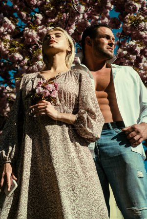 Photo for Fashion couple in pink flowers in summer blossom park. Fashion cosmetics and perfumes - Royalty Free Image