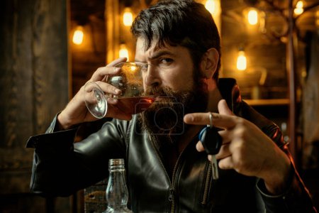 Téléchargez les photos : Un bel homme d'affaires barbu boit du whisky cher. Homme buvant du whisky et tenant ses clés de voiture - en image libre de droit