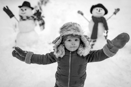 Photo for Little boy playing with snowman in winter park. Outdoor portrait of little son in cold sunny winter weather in park. Winter emotion - Royalty Free Image