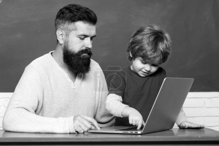Photo for Elementary school teacher and student in classroom. Teacher and schoolboy using laptop in class. Chalkboard copy space. Father and son. Elementary school kid and teacher in classroom at school - Royalty Free Image