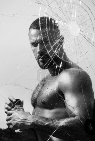 Photo for Strong tattooed man presentating perfume behind breaking window glass. Masculine fragrance for real macho men. Mens power and strength. Mens style and fashion concept - Royalty Free Image