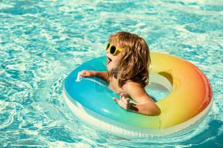 Téléchargez les photos : Vacances d'été pour enfants. Enfant nageant dans la piscine. Les enfants s'amusent à Aquapark. Garçon drôle sur le cercle en caoutchouc gonflable. L'été. Concept d'attractions - en image libre de droit