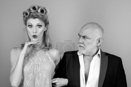 Photo for Difference of ages concept. Couple of younger woman and elder man isolated at orange background. Crafty blonde woman want to marry rich sugar daddy to get his money - Royalty Free Image