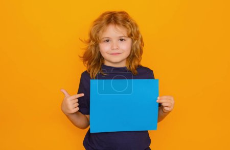 Foto de Kid showing empty sheet of paper, isolated on yellow background. Portrait of a kid holding a blank placard, poster. Copy space - Imagen libre de derechos