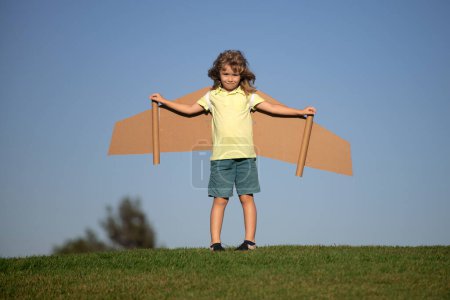 Téléchargez les photos : Drôle de garçon avec des ailes d'avion en carton jouet voler. Concept de liberté de démarrage. Enfant portant un costume d'aviateur extérieur. Imagine peu de rêves de pilote de voler - en image libre de droit