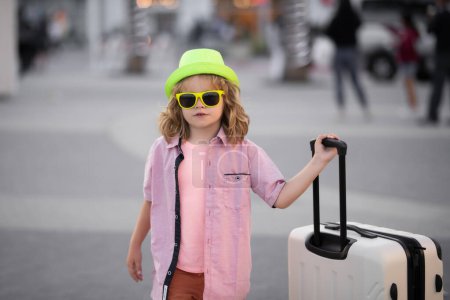 Foto de Niño turista viajero en ropa casual, gafas de sol de moda y sombrero sostienen maleta. Viaja al extranjero los fines de semana. Viajes y aventura - Imagen libre de derechos