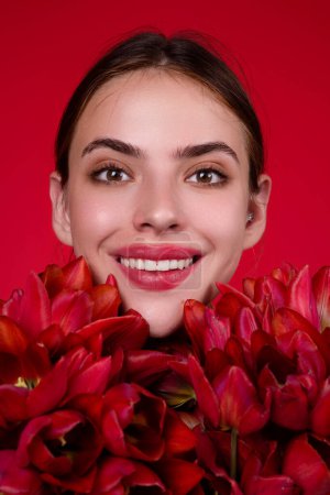 Photo for Happy smilig woman with flowers. Beauty girl with tulip. Beautiful sensual woman hold tulips bouquet, studio portrait on red background. Close up beauty woman face near tulips bouquet - Royalty Free Image