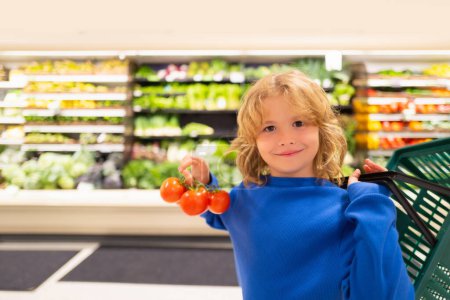 Foto de Niño con verduras frescas de tomate. Retrato de niño en una tienda de alimentos o un supermercado. Un niño yendo de compras. Comida saludable para niños - Imagen libre de derechos