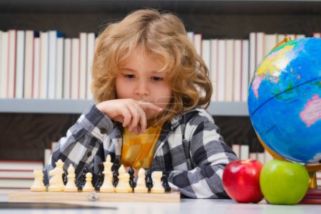 Téléchargez les photos : Un gamin joue aux échecs à l'école. Chess for intelligent kid. Génie de l'enfant, élève intelligent jouant au jeu de société logique. Intelligent écolier penser aux échecs - en image libre de droit