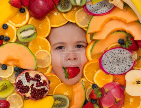 Téléchargez les photos : Strawberry in child mouth. Frutit and child face close up. Top view of child face with mix fruit. Fruits set near kids face - en image libre de droit