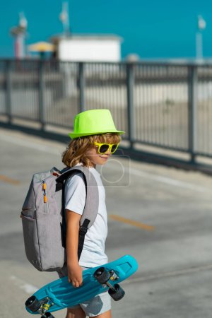 Photo for Childhood. Cute child with skateboard on street background. Summer outdoor sport. Funny kid boy, stylish skater holding skateboard outdoor. Fashion child in summer shirt stylish hat and sunglasses - Royalty Free Image