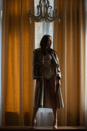 Téléchargez les photos : Femme de mode sexy et sensuelle dans un appartement de luxe posant sur des rideaux de fenêtre. séduisante sexy belle jolie jeune femme sensuelle avec un corps mince parfait posant sur fond de studio - en image libre de droit