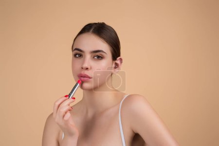 Photo for Beautiful young woman applying red lipstick on lips, studio color background. Sexy girl applied lipstick. Young nodel holding pink lipstick. Red lips make up. Beautiful woman putting lipstick on lips - Royalty Free Image