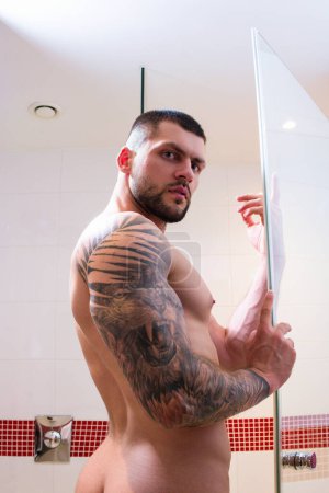 Foto de Hombre musculoso sexy tomando ducha en el baño. Tipo sexy lavando cuerpo desnudo. Cuidado corporal masculino, rutina de belleza e higiene diaria. Gay con torso desnudo en el baño. Rutina. Fresco por la mañana - Imagen libre de derechos