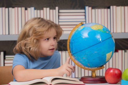 Foto de School pupil looking at globe in library, geography lesson. School child studying in classroom at elementary school. Kid studying on lesson in class at elementary school - Imagen libre de derechos