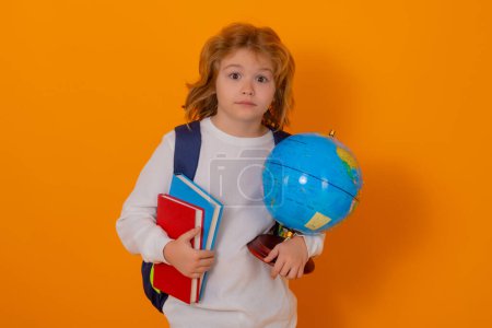 Téléchargez les photos : Pupil, nerd schoolboy. School boy hold world globe and book, isolated on yellow studio background. School and kids. Cute blonde child with a book learning. Knowledge day - en image libre de droit