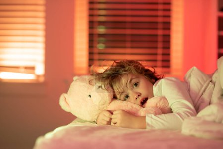Foto de Niño asustado en la cama. Niño en la cama con juguete osito de peluche. Pesadilla para los niños. Siesta y hora de dormir. Ropa de cama y ropa de dormir para niños - Imagen libre de derechos