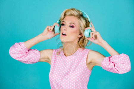 Foto de Imagen de una mujer rubia sorprendida escuchando música con auriculares aislados sobre el fondo del estudio. Chica joven emocionada con auriculares escuchando música y dancind - Imagen libre de derechos