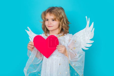 Téléchargez les photos : Enfant ange avec cœur. Les enfants de Noël. Petit ange Cupidon enfant avec des ailes. Portrait studio de gosse angélique - en image libre de droit