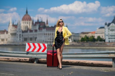 Téléchargez les photos : Touristique femme sexy à Budapest. Femme touristique en robe de mode avec valise marchant dans la rue. Fille étudiante voyageur portrait extérieur. Femme touristique ayant voyage de vacances - en image libre de droit