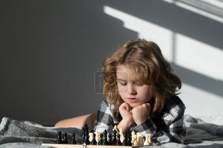 Téléchargez les photos : Enfant jouant aux échecs à la maison. Un gamin qui joue aux échecs. Un enfant intelligent qui pense aux échecs. Développement précoce des enfants - en image libre de droit
