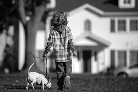 Téléchargez les photos : Enfant et chiot dehors. Joyeux garçon et chien jouant à la pelouse. Animaux marchant - en image libre de droit