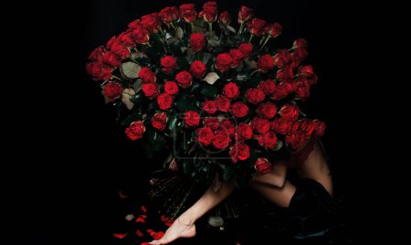 Téléchargez les photos : Beauté femme romantique avec des fleurs de Rose Rouge. Fleurs préférées. Fille heureuse étreint un bouquet. Saint Valentin. Belle femme séduisante tenant un grand bouquet de roses rouges sur fond noir - en image libre de droit