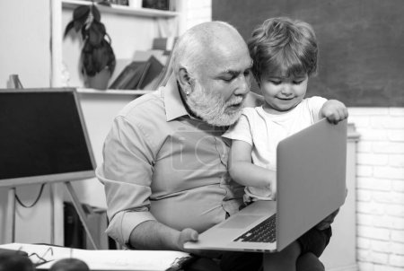 Foto de Concepto de educación y lectura. Abuelo con nieto aprendiendo juntos. Feliz nieto lindo y abuelo sentado en un escritorio en el interior - Imagen libre de derechos
