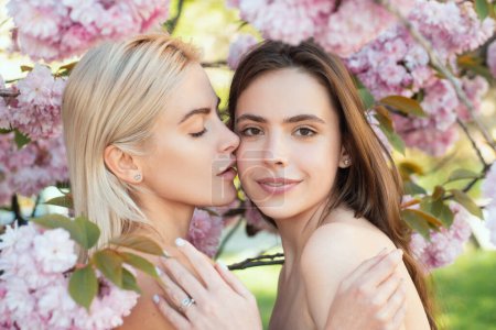 Foto de Retrato de dos hermosas chicas primaverales. Dos mujeres jóvenes relajándose en flores de sakura. Una pareja de lesbianas besándose. Tacto y beso sensual. Novia. - Imagen libre de derechos