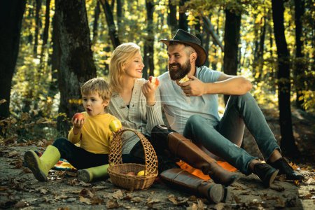 Photo for Cheerful family sitting on the grass during a picnic in a park. Young smiling family doing a picnic on an autumns day. Happy family in the park evening light. Autumn family picnic concept - Royalty Free Image