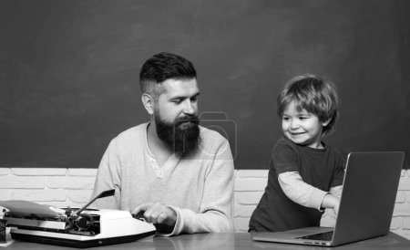 Foto de Teacher helping young boy with lesson. First day in school. Teacher helping kids with their homework in classroom at school. Daddy and son together. Back to school. Child learning - Imagen libre de derechos