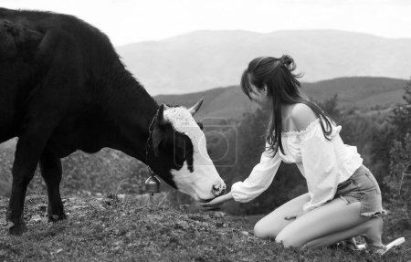 Foto de Mujer alimentando vaca. Chica granjera con vaca Holstein en el prado. FarmerVegan, concepto vegetariano. Toma vegetales. Estilo de vida saludable, leche de campo orgánica - Imagen libre de derechos
