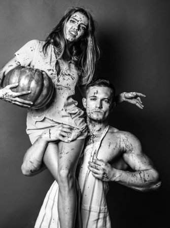 Téléchargez les photos : Jeune zombie couple homme à poitrine nue et vampire femme dans le sang et Halloween maquillage tenant citrouille isolé fond rouge. Concept de célébration des fêtes. Affiche Halloween - en image libre de droit