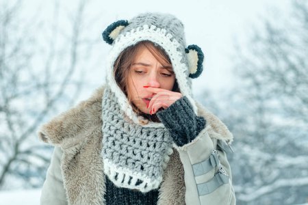 Téléchargez les photos : Grippe froide saison hivernale, nez qui coule. Montrant femme malade éternuer au parc d'hiver - en image libre de droit