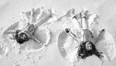 Foto de Dos niñas haciendo ángel de nieve mientras yacen en la nieve. Chica feliz en un ángel de nieve muestra - Imagen libre de derechos