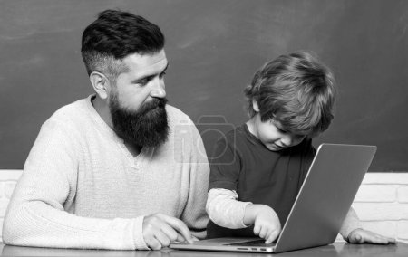 Foto de Young boy doing his school homework with his father. Teacher helping young boy with lesson. Little students. Daddy and son together. Back to school - Imagen libre de derechos