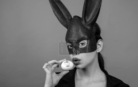 Photo for Sexy woman wearing a black Easter Bunny. Female mouth kiss. Red lip imprint on easter egg on red background - Royalty Free Image