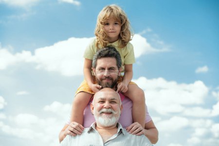 Téléchargez les photos : Portrait d'hommes génération grand-père père et petit-fils en plein air sur le ciel. Concept de fête des pères. Des hommes d'âges différents. Hommes drôles visages - en image libre de droit