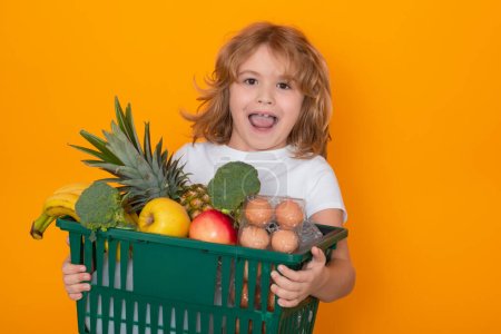 Photo for Food store. Excited child hold shopping cart full of groceries. Kid holds shopping basket over yellow background. Store, shopping, sales and discounts - Royalty Free Image