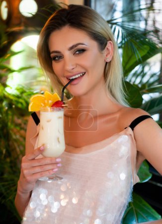 Téléchargez les photos : Sensual woman wearing a white cocktail dress drinking a tropical cocktail. Pina colada. Cocktail party - en image libre de droit